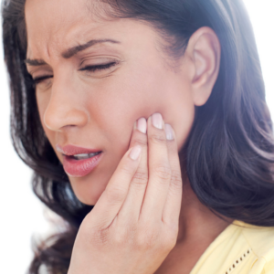 Woman experiencing jaw pain, clutching her jaw in discomfort, highlighting the symptoms of TMJ disorders.